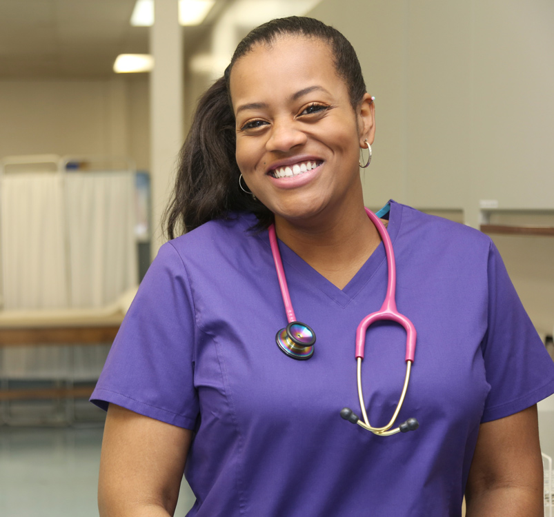 A clinical medical assistant smiles in front of her clinical office